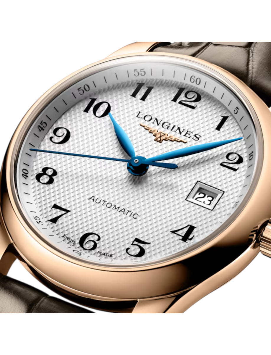 Gold watch with white textured dial, blue hands, and date window showing 23, Longines automatic label