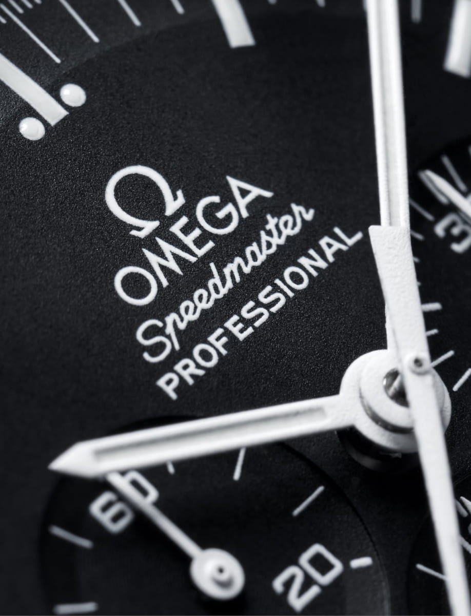 Close-up of an Omega Speedmaster Professional watch dial with white hands and a black textured face.