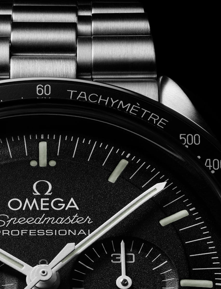 Close-up of an Omega Speedmaster Professional watch dial, showing the tachymeter bezel and chronograph hands.