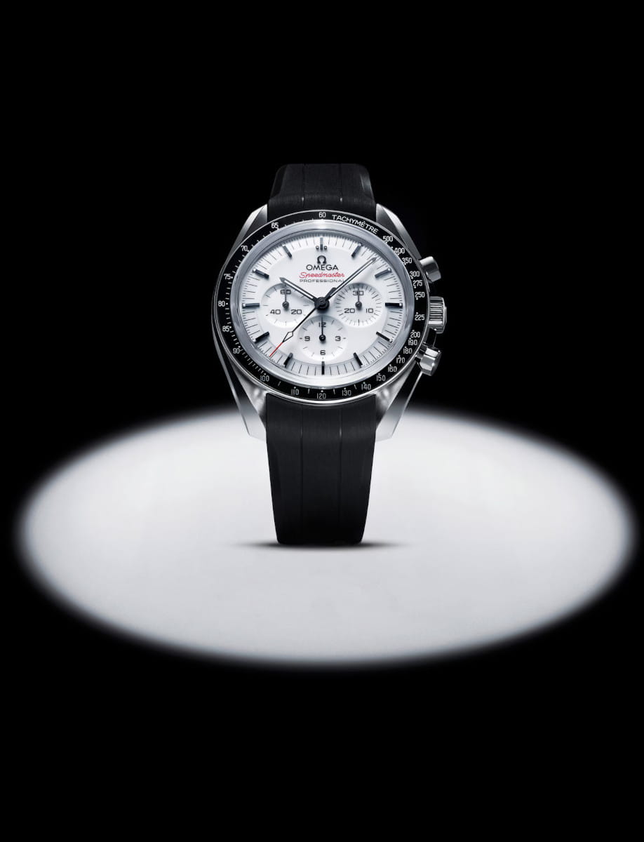 Omega Speedmaster chronograph watch with white dial and black strap illuminated by a spotlight on a dark background.