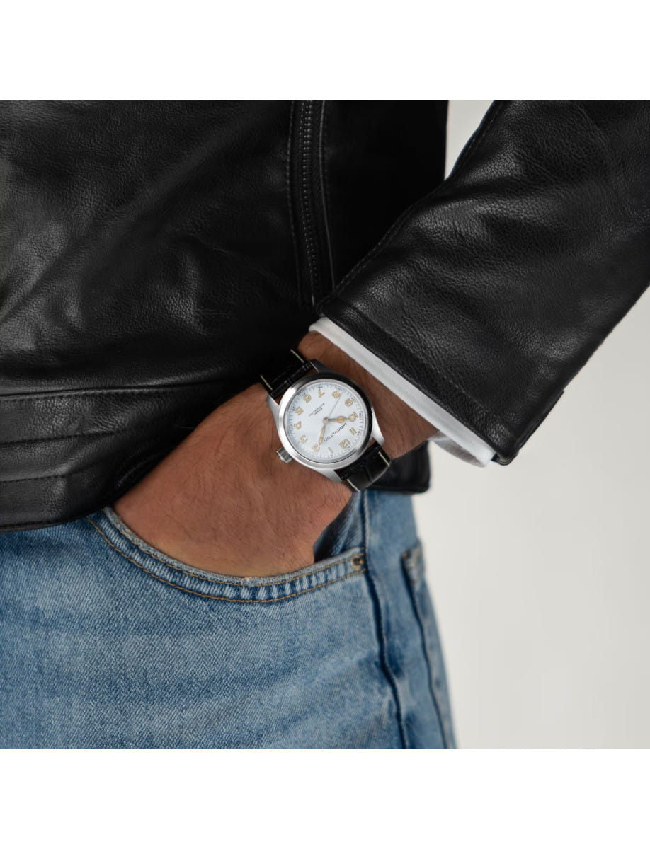 Close-up of a wrist wearing a stainless steel watch with a white dial, paired with a black leather jacket and blue jeans