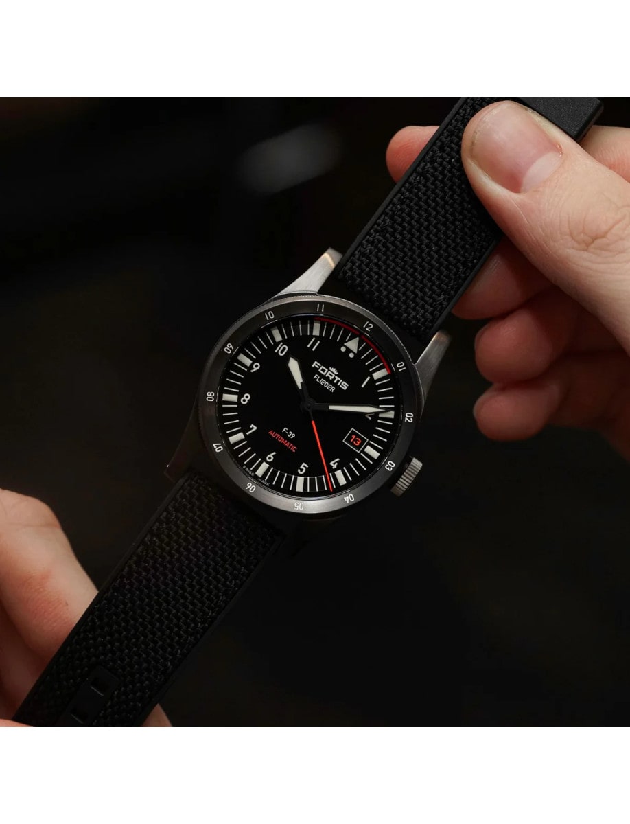 A wristwatch with a recycled stainless steel case coated in black DLC, a matte black dial, and a hybrid rubber/textile fabric strap.