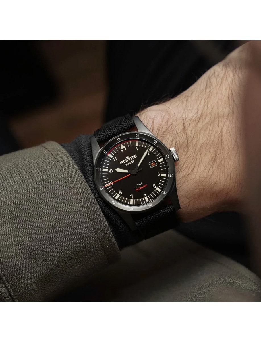 A wristwatch with a recycled stainless steel case coated in black DLC, a matte black dial, and a hybrid rubber/textile fabric strap.