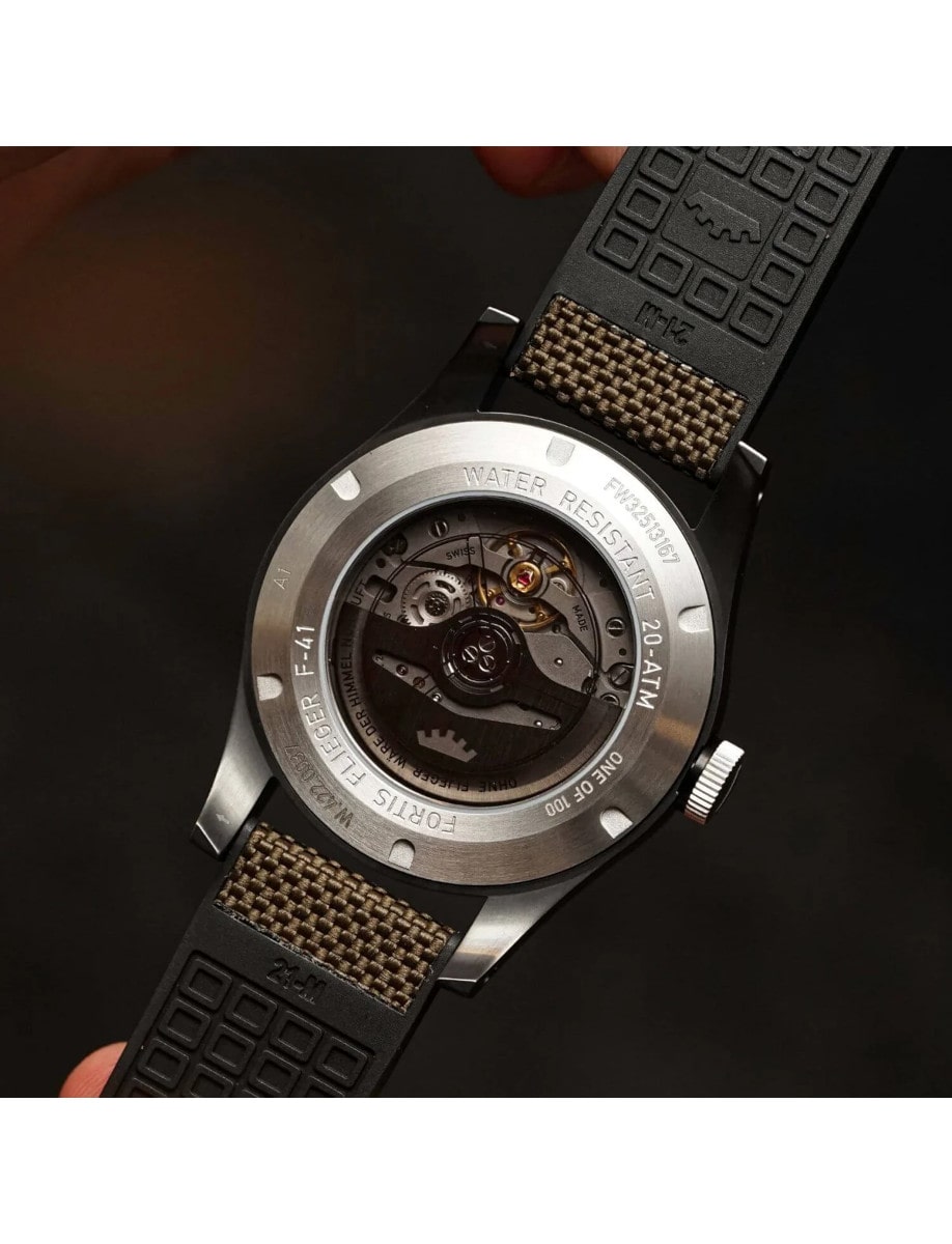 Case back view of a wristwatch with a recycled stainless steel case coated in black DLC and a hybrid rubber/textile fabric strap, showing the automatic movement.