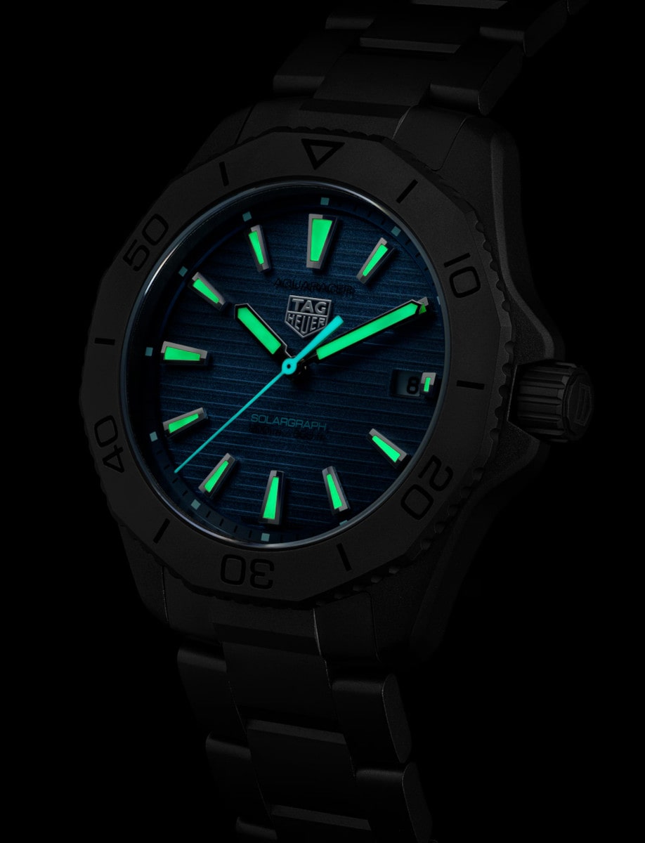Night view of Tag Heuer wristwatch with titanium case and bracelet, and blue dial with luminous hands and markers.