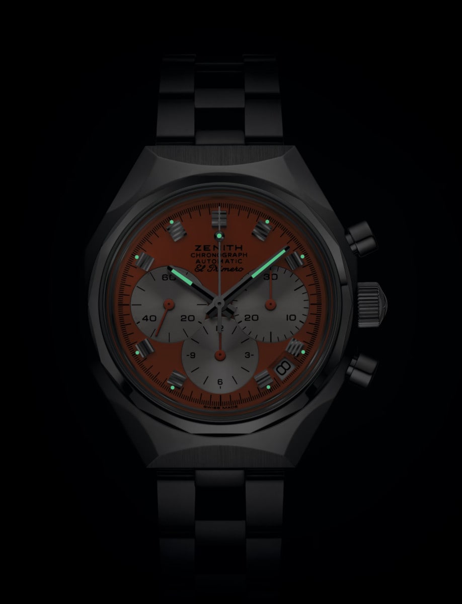 Night view of Zenith wristwatch with stainless steel case and bracelet, and orange dial.