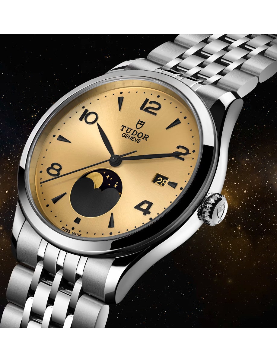 Side view of Tudor wristwatch with stainless steel case and bracelet, and champagne-color satin sun-brushed dial with applied numerals and moon phase indicator.