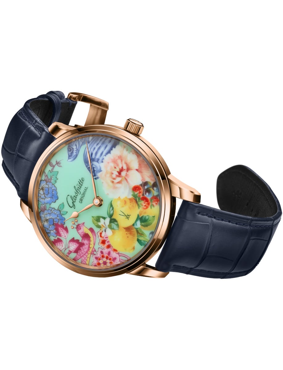 Side view of Glashutte Original wristwatch with red gold case, collage motif MEISSEN porcelain dial, and blue Louisiana Alligator leather strap