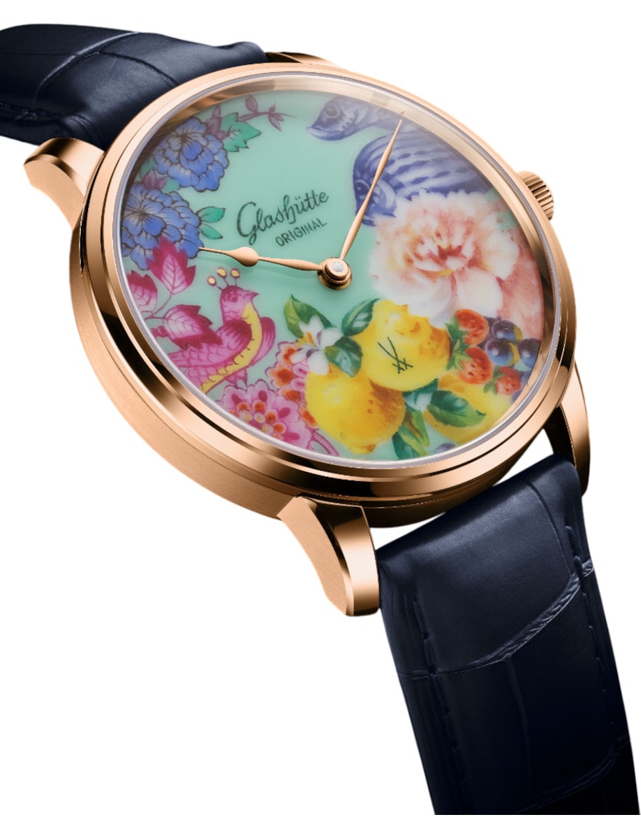 Side view of Glashutte Original wristwatch with red gold case, collage motif MEISSEN porcelain dial, and blue Louisiana Alligator leather strap