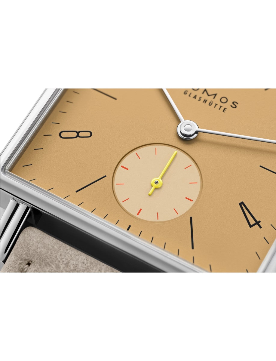 Close view of Nomos wristwatch with stainless steel case, ocher yellow dial, and vegan velour remborde beige strap.