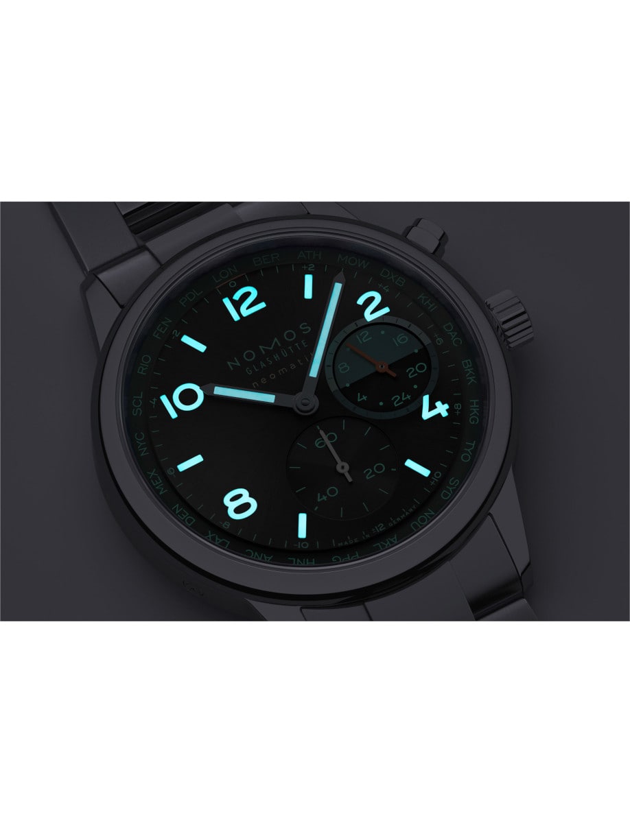 Night view of Nomos wristwatch with stainless steel case and bracelet, black dial with turquoise accents, and luminous hands and hour markers.