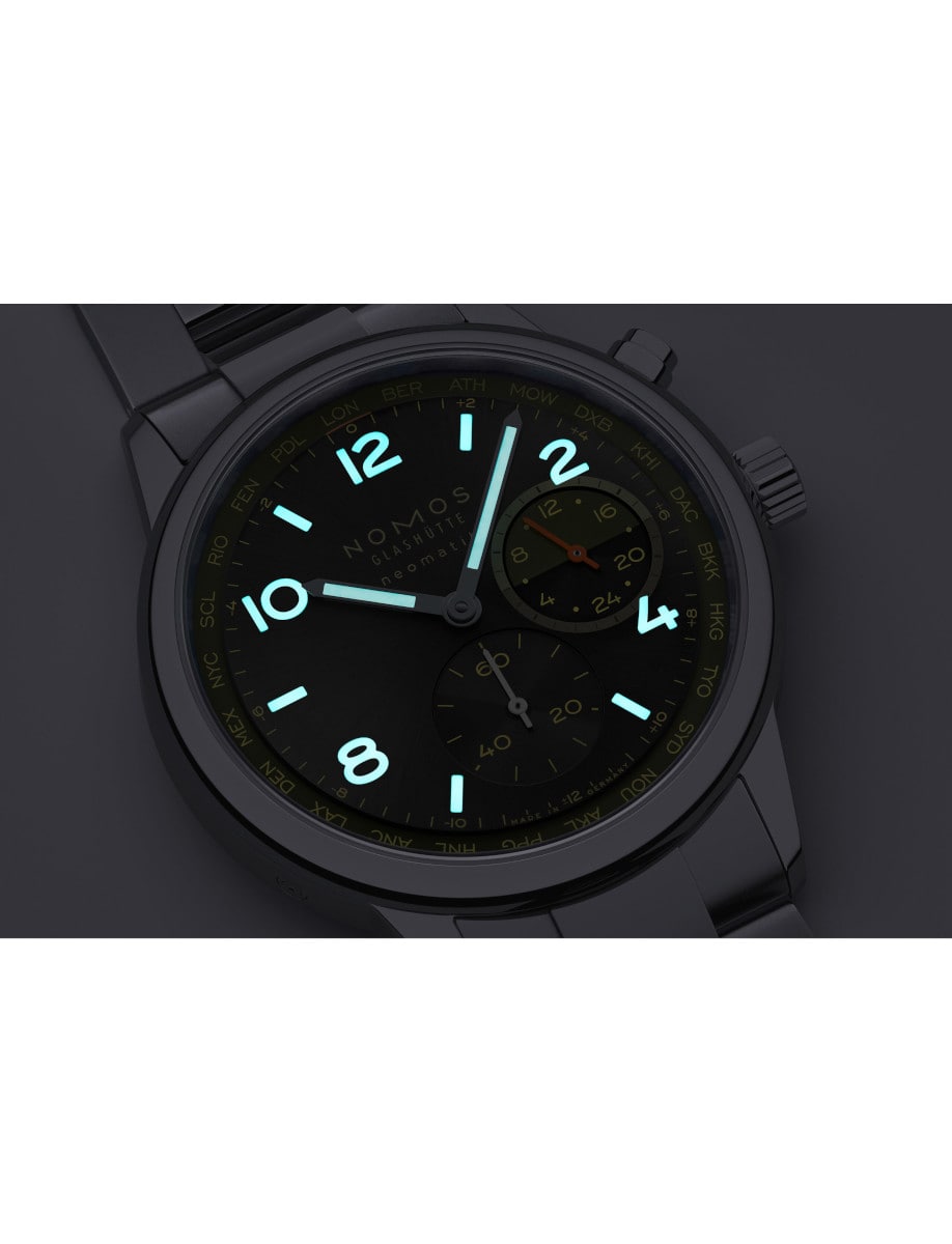 Night view of Nomos wristwatch with stainless steel case and bracelet, black dial with light yellow accents, and luminous hands and hour markers.