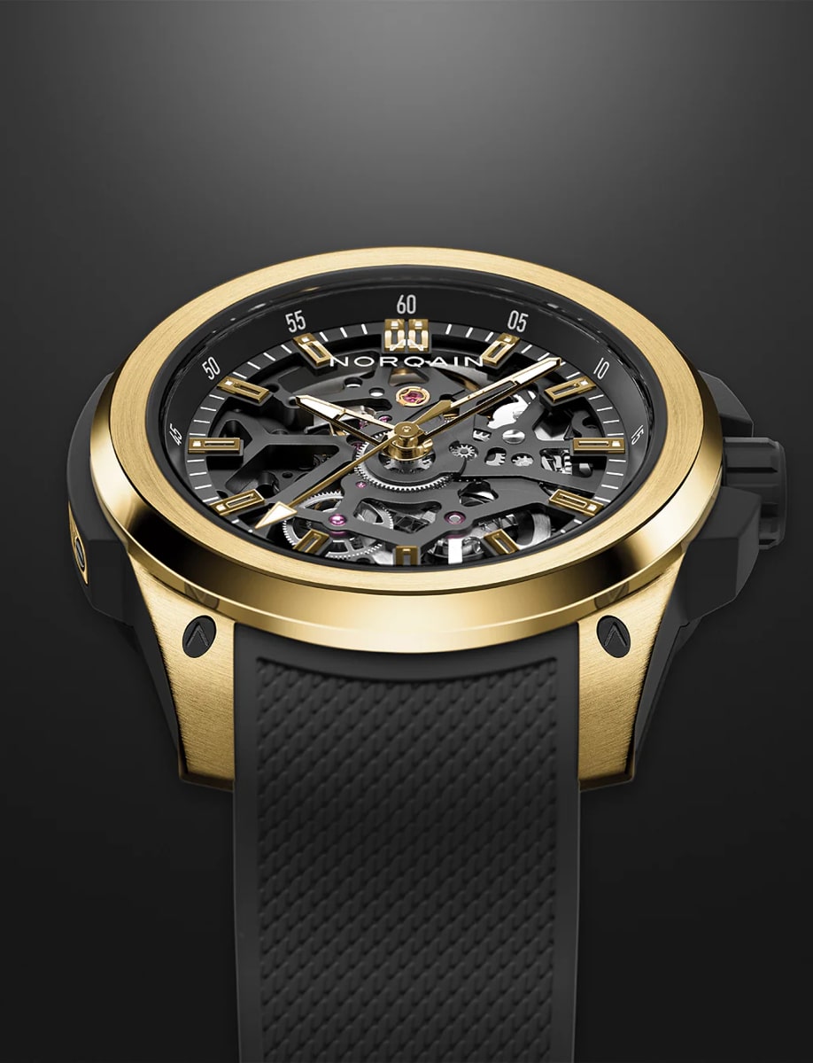 Front side view of Norqain wristwatch with yellow gold case, openworked black dial and black rubber strap