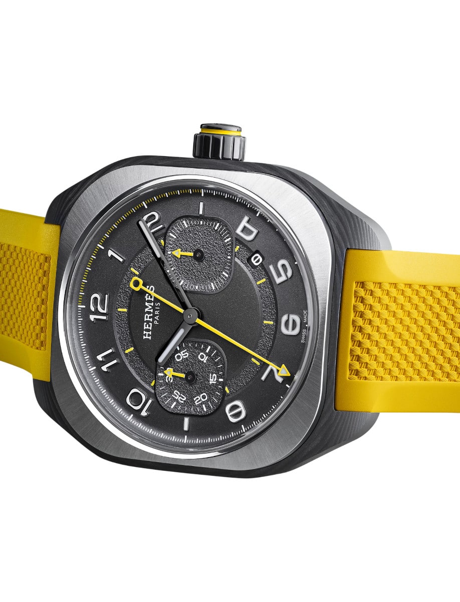 Side view of Hermes wristwatch with carbon fiber composite case, black gold treated and blackened dial, and Naples yellow rubber strap.