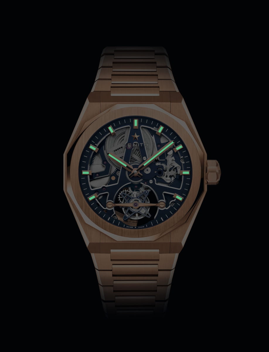 Night view of Zenith wristwatch with solid rose gold case and bracelet, and blue openworked dial with luminous hands and markers.