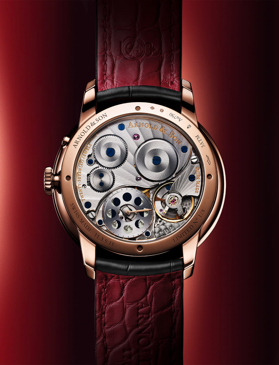 Back view of Arnold&Son wristwatch with 18k red gold case, open case back, and black leather strap.