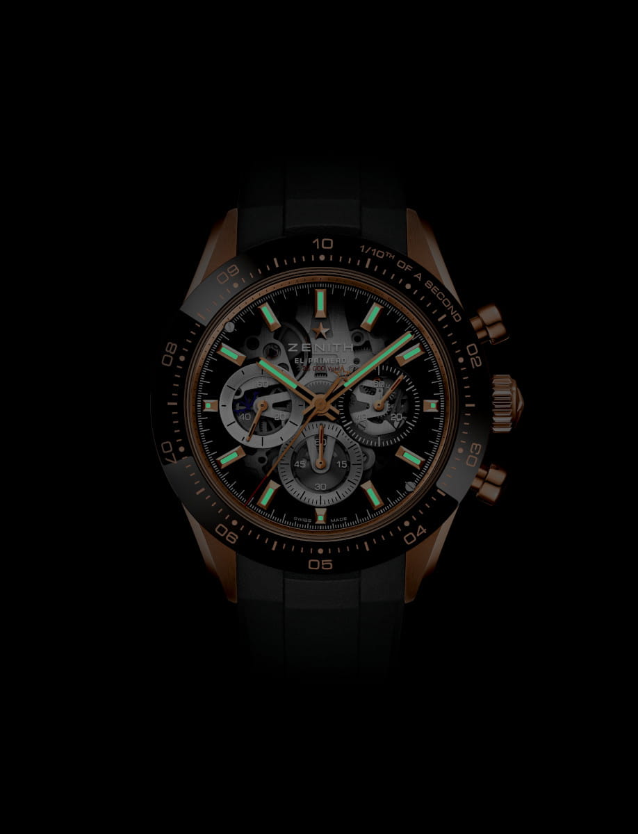 Night view of Zenith Chronomaster Sport Skeleton wristwatch with 18k rose gold case with black ceramic bezel, openworked dial with tinted sapphire with three different-coloured counters, and black rubber strap.
