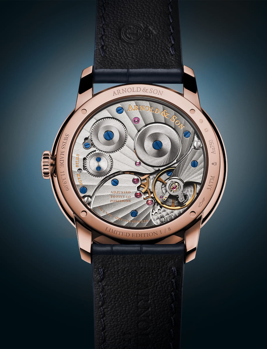 Back view of Arnold&Son HM Pietersite wristwatch with 18k red gold case, sapphire crystal case back, and ink blue alligator leather strap.