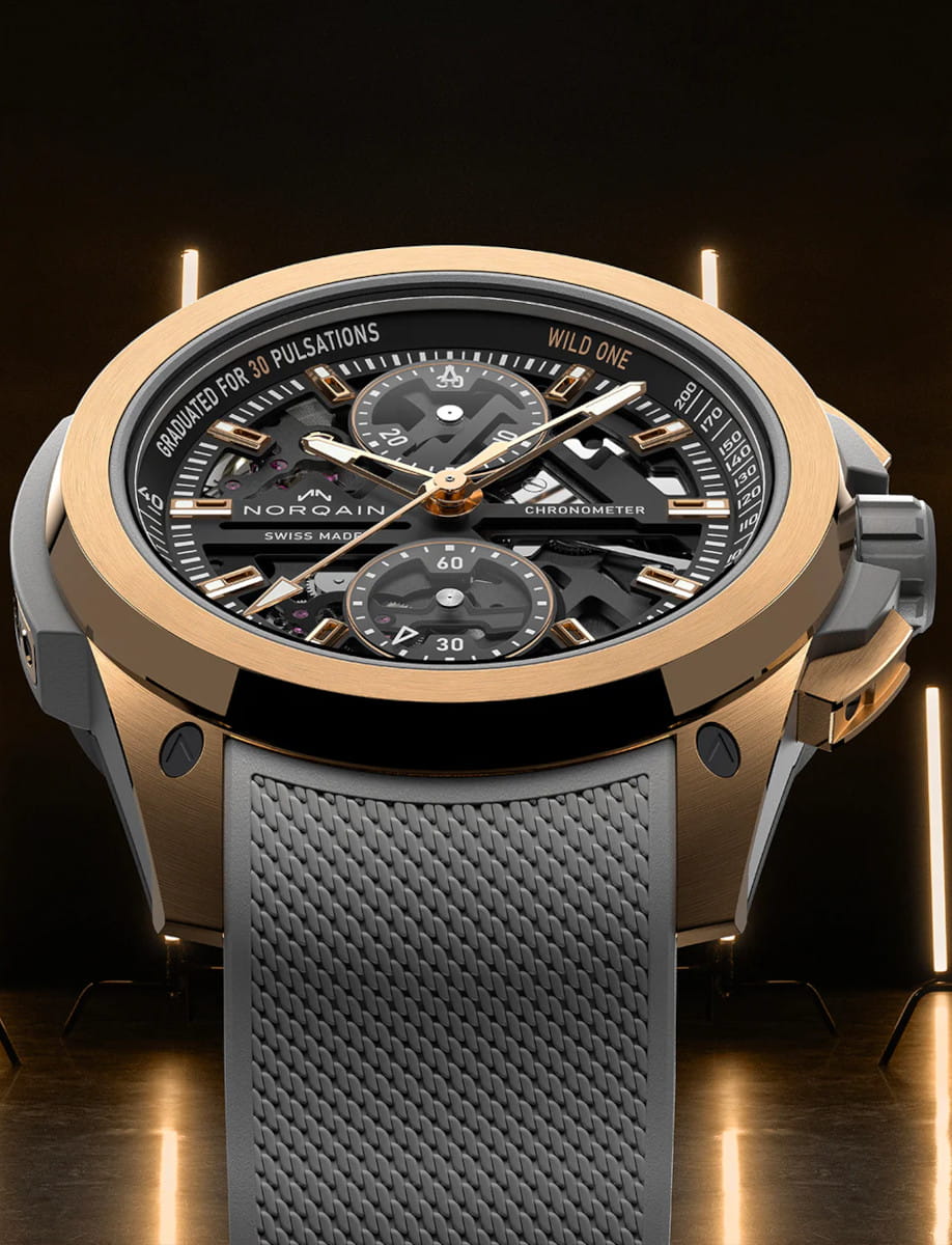 Front view of Norqain Wild ONE Skeleton Chrono Red Gold wristwatch with 18k 5N “PX IMPACT®” red case, black dial with white and gold printings, grey rubber strap with “Milanese” pattern.