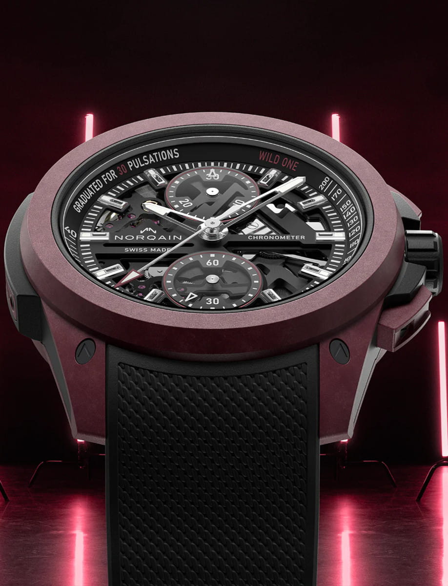 Front side view of Norqain Wild ONE Skeleton Chrono wristwatch with Burgundy NORTEQ titanium case, black dial with white and burgundy printings, black rubber strap with “Milanese” pattern.