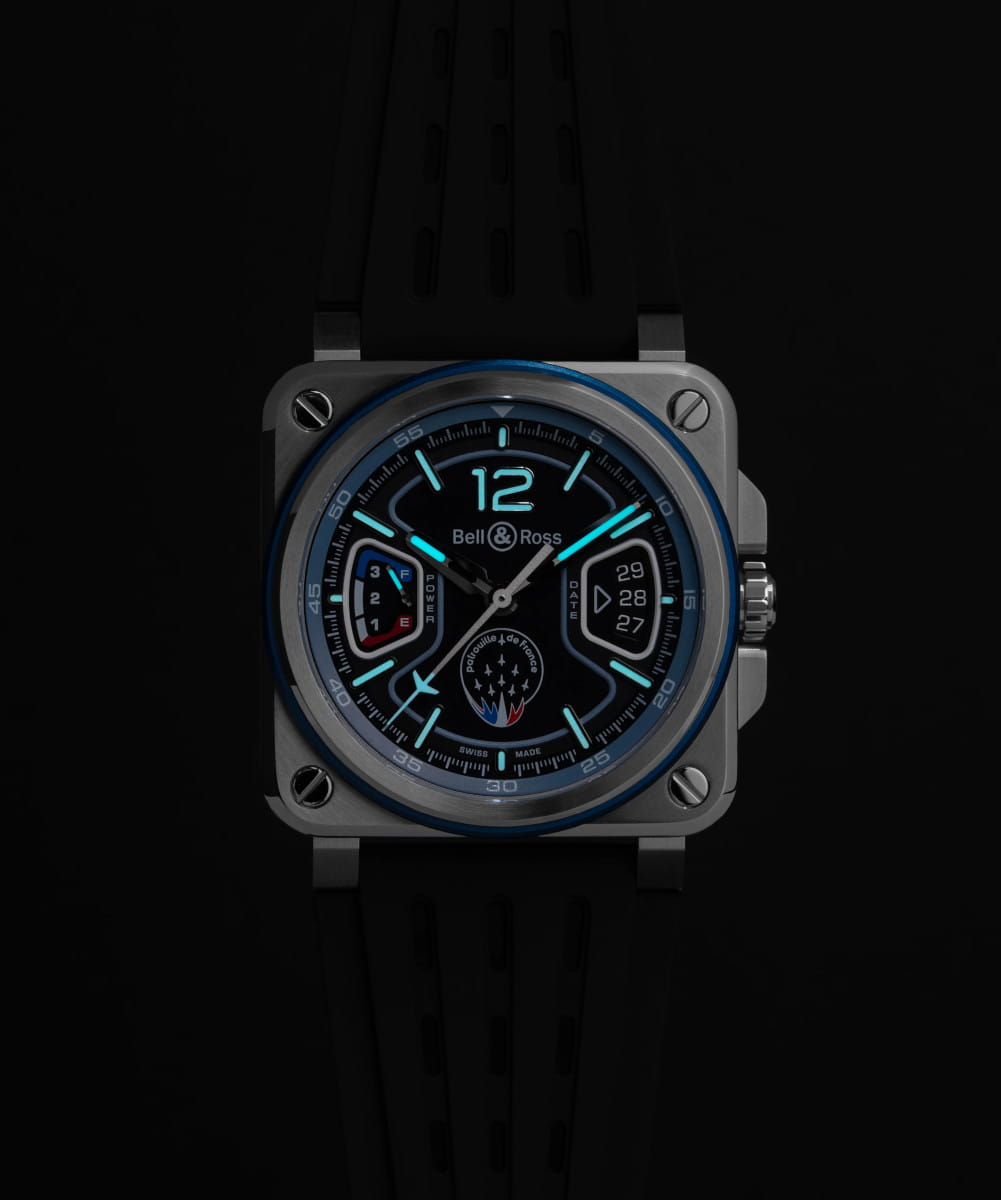 Night view of Bell&Ross BR-X3 Patrouille de France wristwatch with stainless steel case, black rubber strap, and matt black base dial with blue and white skeletonised applique.
