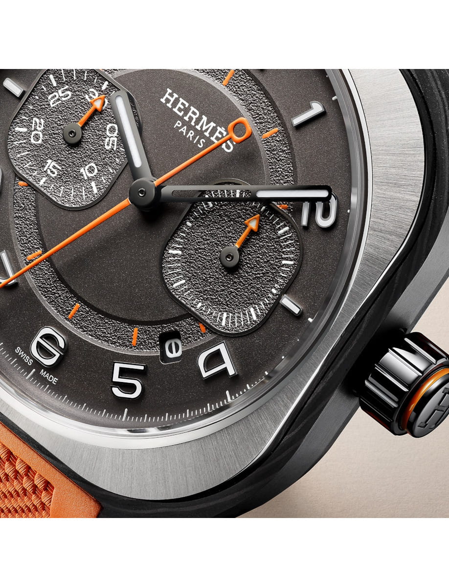 Close view of Hermes wristwatch with carbon fiber composite case, black gold treated and blackened dial, and orange rubber strap.