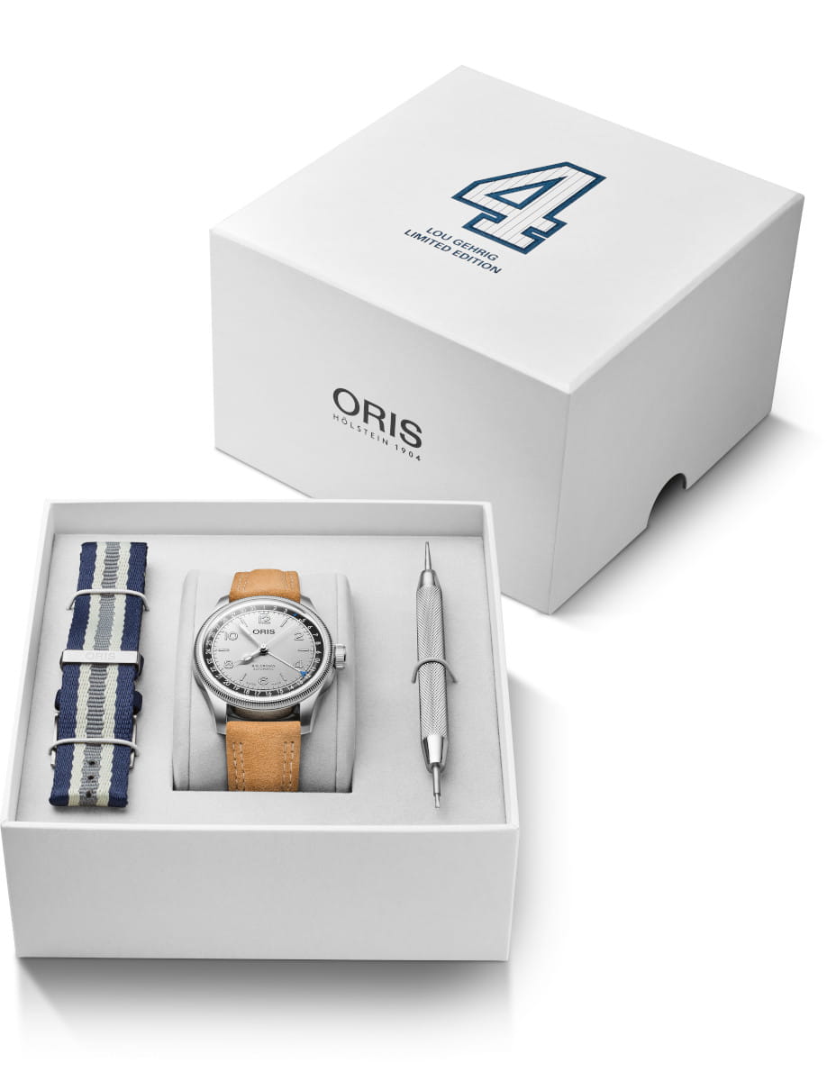 Box view of Oris Lou Gehrig Limited Edition wristwatch with stainless steel, silver dial, brown leather strap and additional blue, white and grey NATO fabric strap.