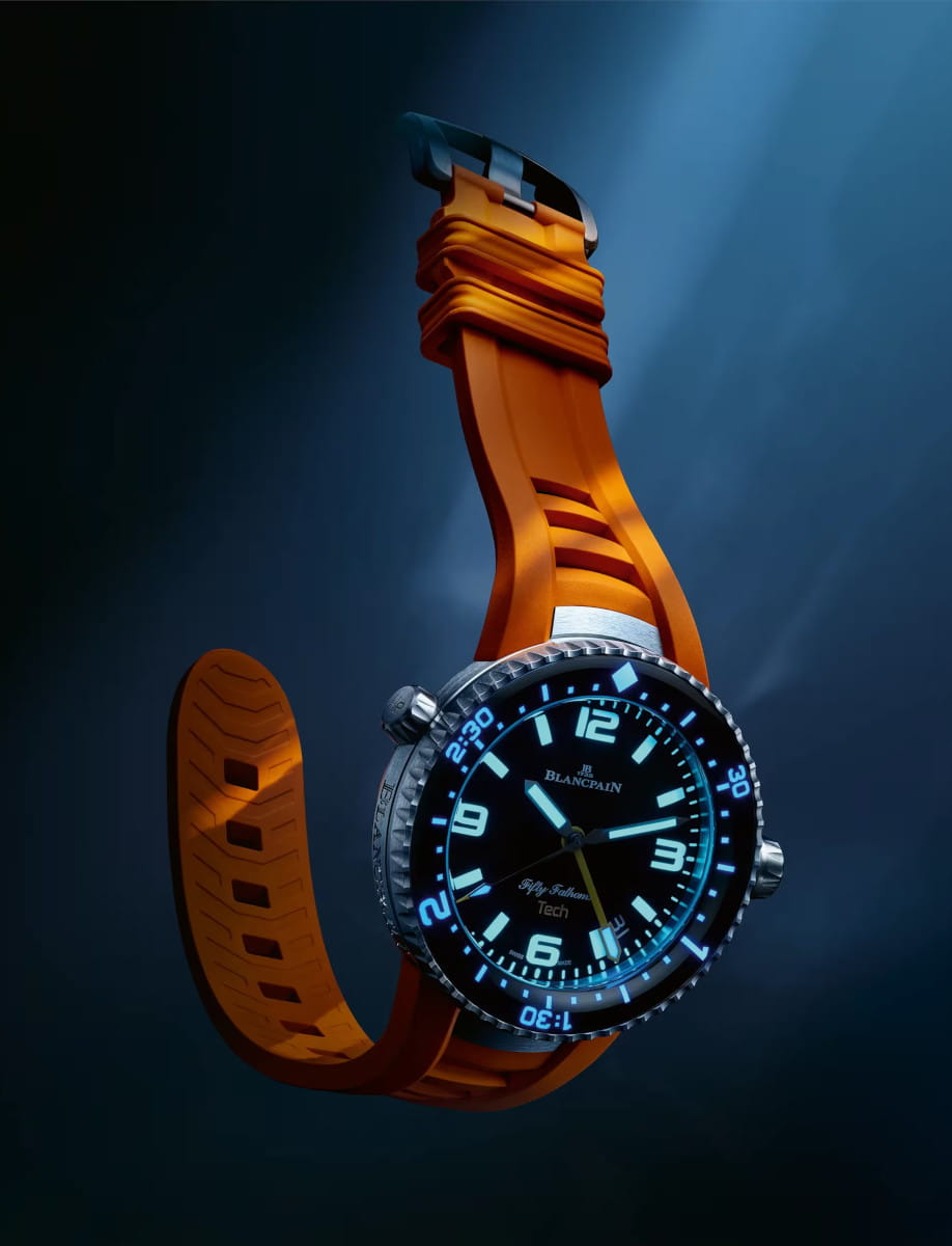 Night view of Blancpain Fifty Fathoms wristwatch with titanium case, black dial, and orange rubber strap.