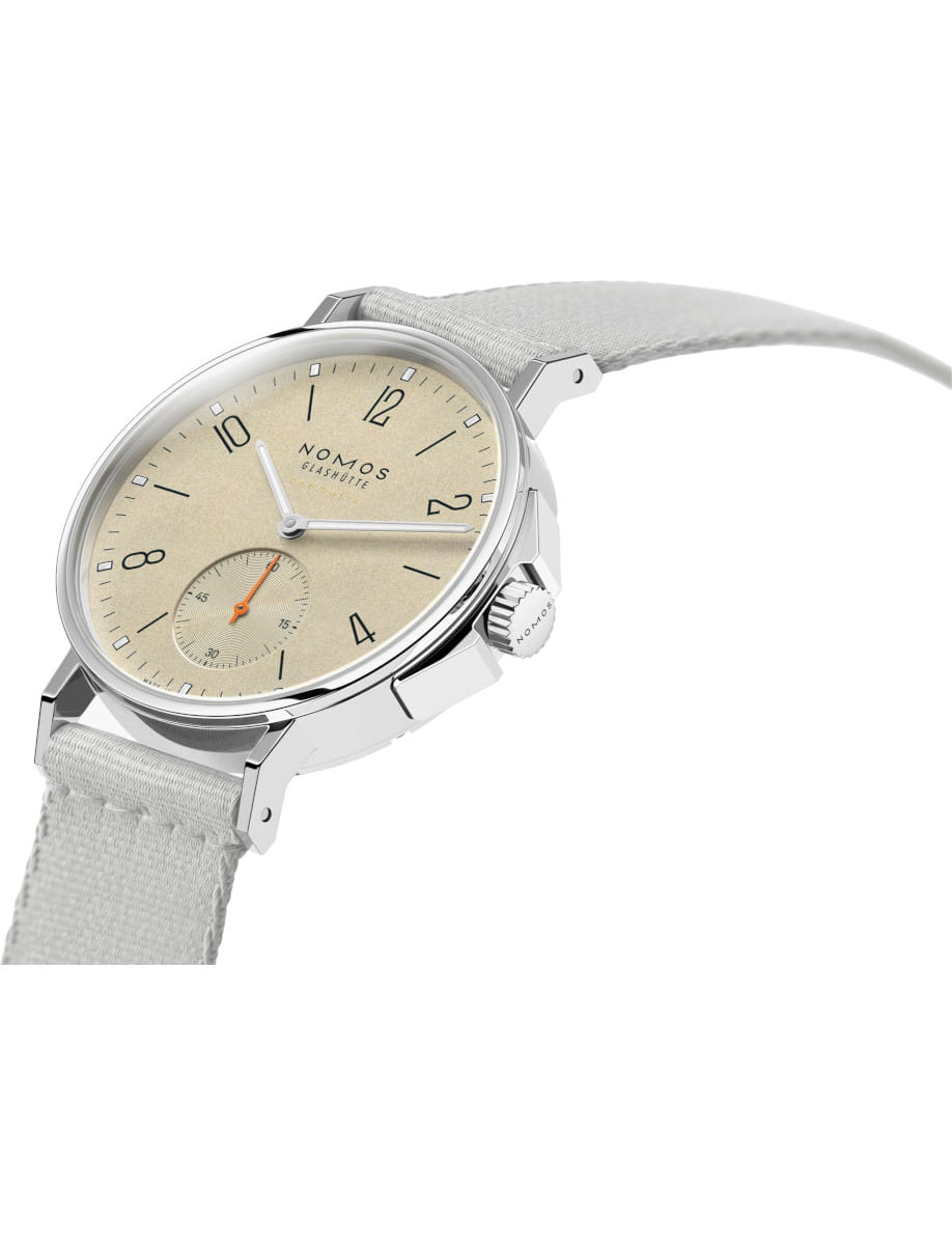 Nomos Glashütte wristwatch with beige dial, silver case, and light fabric strap seen at an angled view.