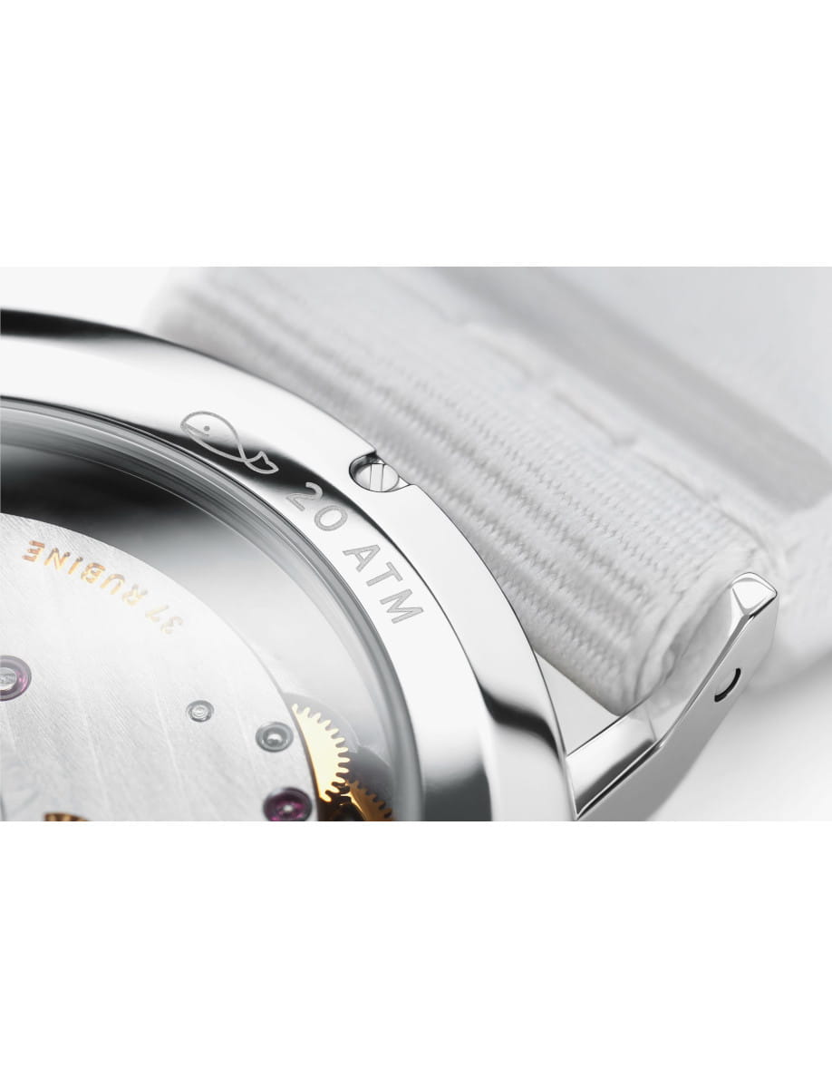 Close-up of a stainless steel wristwatch with a transparent case back revealing gears and the movement, attached to a light fabric strap.