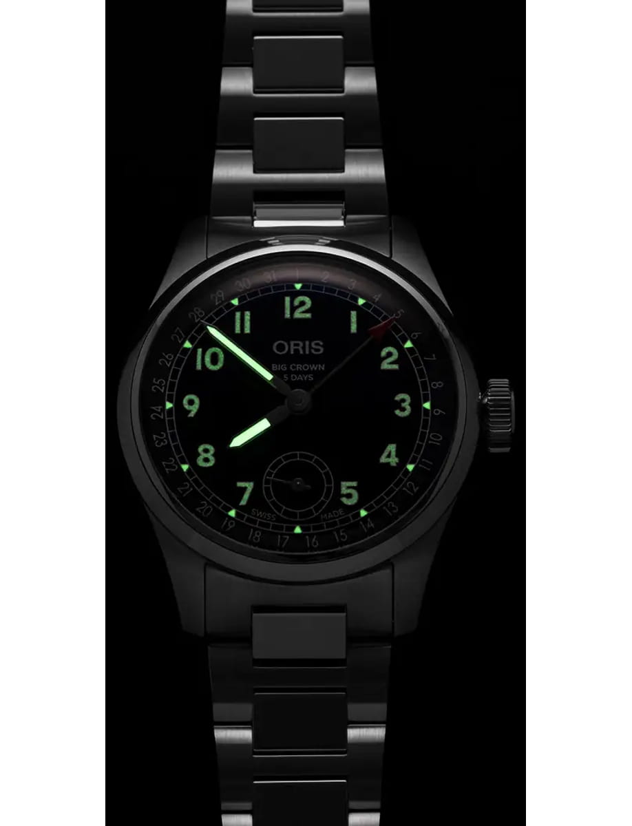 Oris Big Crown wristwatch with a black dial, glowing green numerals, and a stainless steel bracelet.