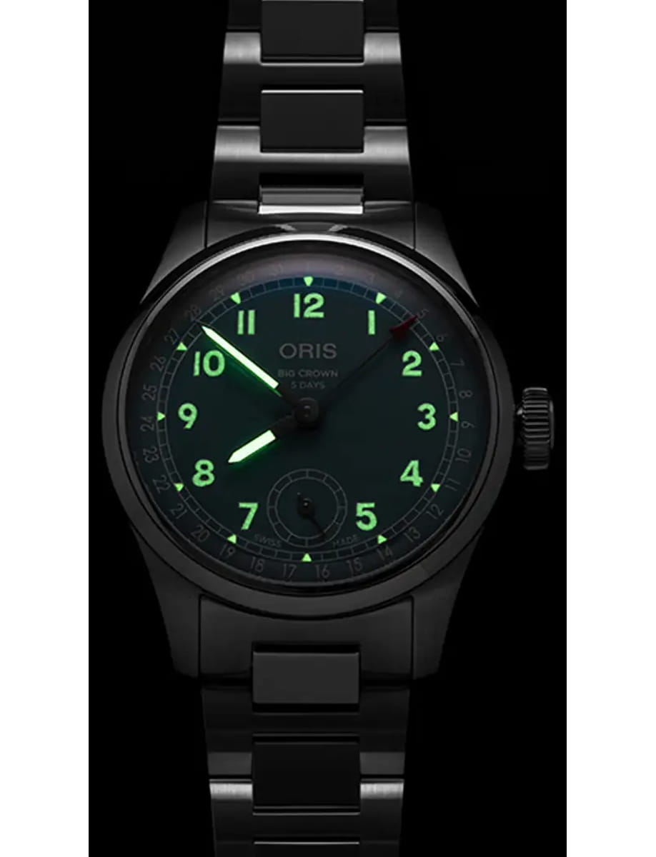 Black stainless steel Oris wristwatch with glowing green numerals and hands, close-up of dial and bracelet.