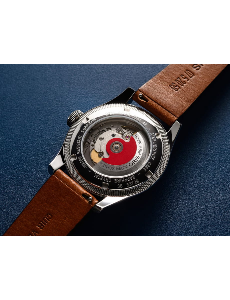 Close-up of a stainless steel wristwatch with a see-through case back, red rotor and intricate gears, brown leather strap visible on blue background.