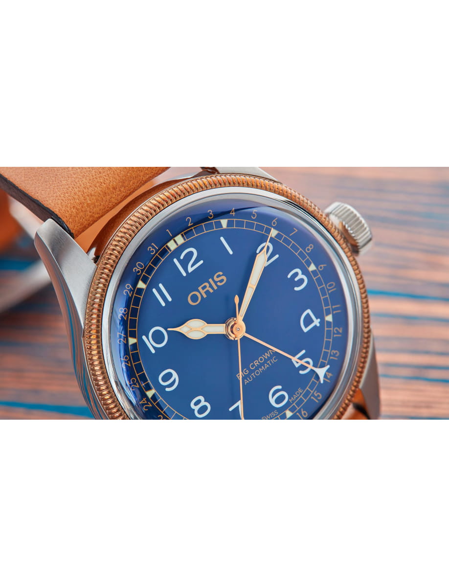 Close-up of a blue-dial Oris wristwatch with a gold bezel and tan leather strap