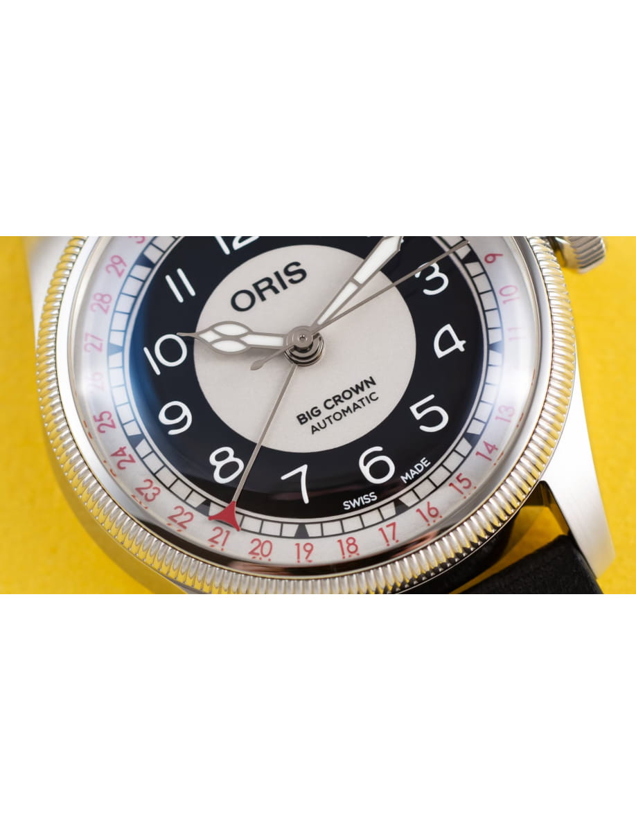 Oris Big Crown automatic wristwatch with black-and-silver dial and red numeral ring on a yellow background