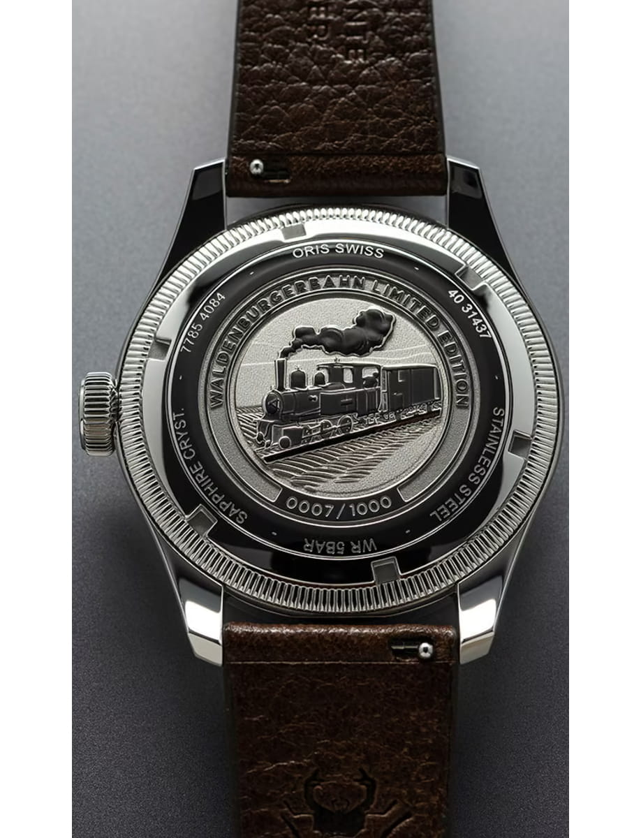Close-up of the back of a stainless steel wristwatch showing an engraved steam locomotive design and a brown leather strap, highlighting the mechanical details around the case back.