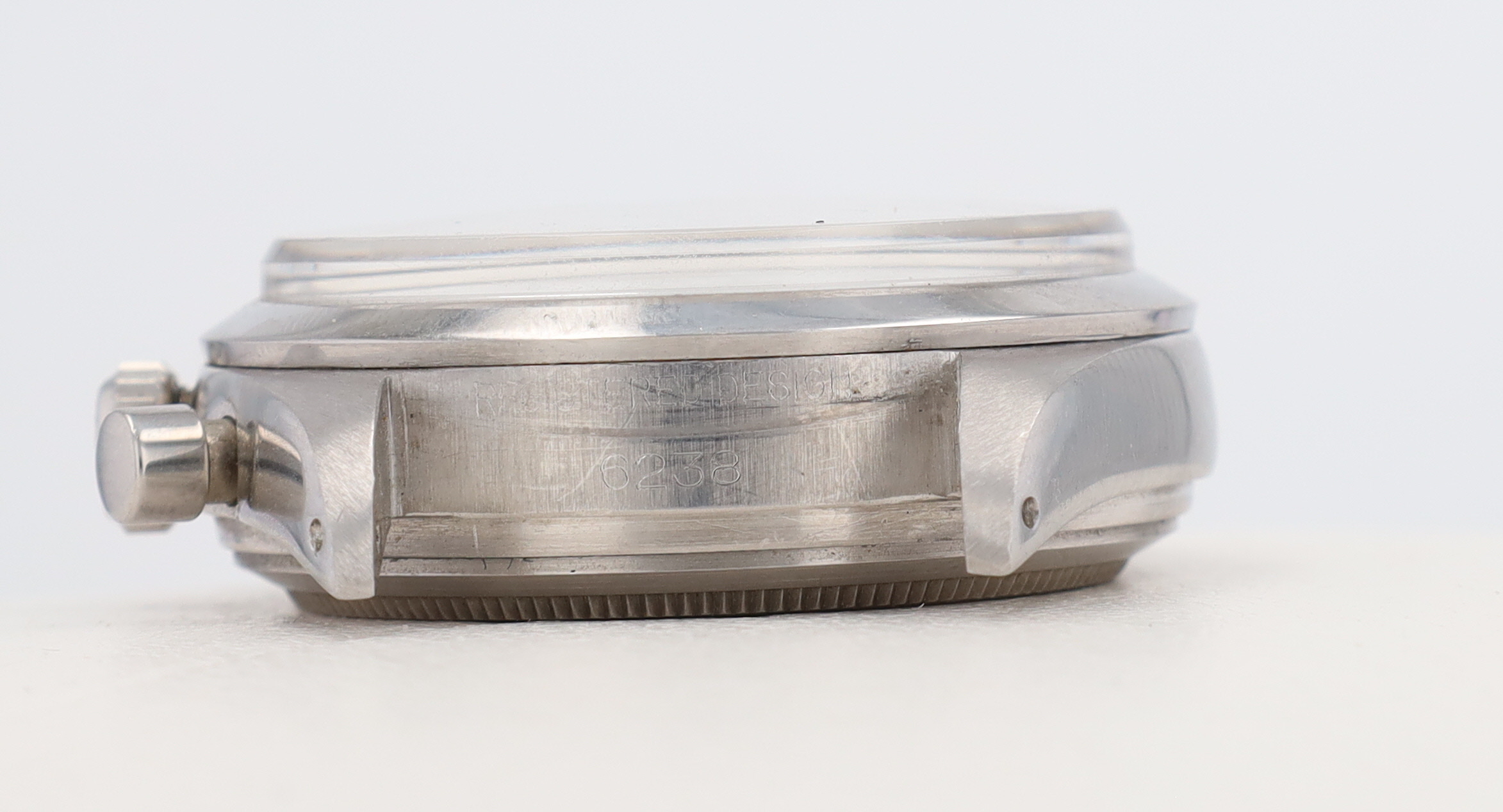 Close-up of a silver vintage wristwatch case laid flat, showing the side crown and worn edge details