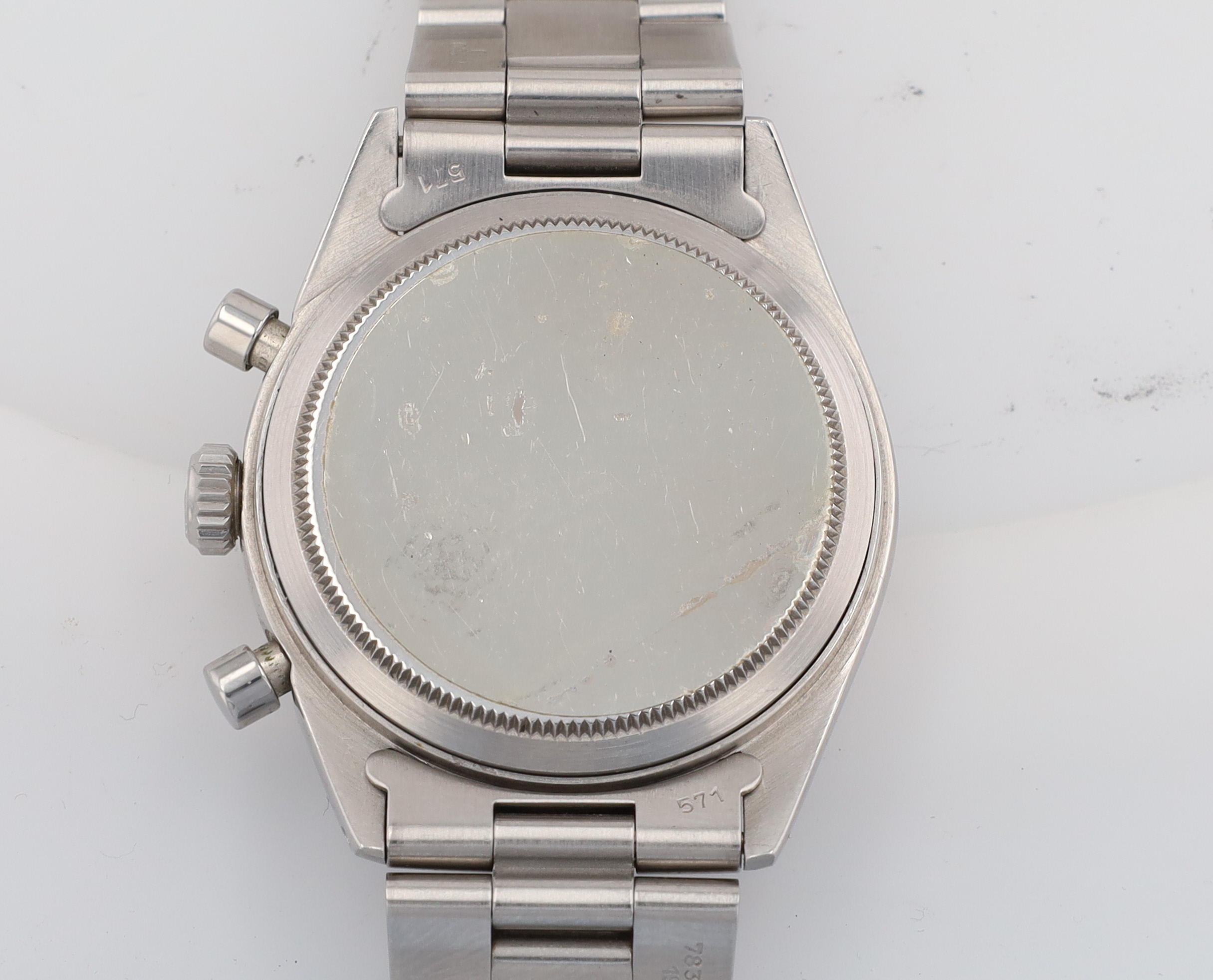 Close-up of a stainless steel wristwatch case back with a knurled edge and metal bracelet links visible above and below.