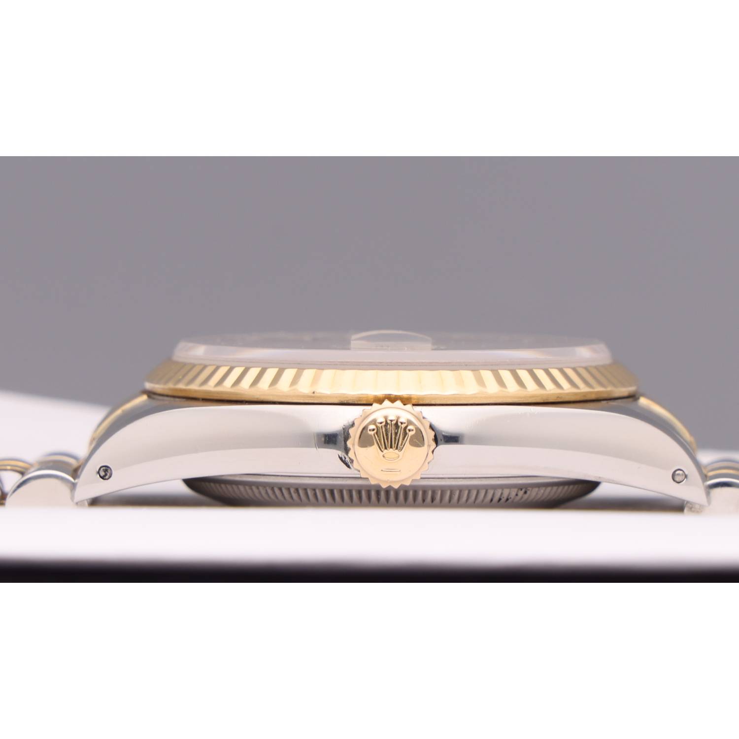 Close-up of a two-tone Rolex watch crown with the crown logo, set against a fluted gold bezel and polished metal case, side view.