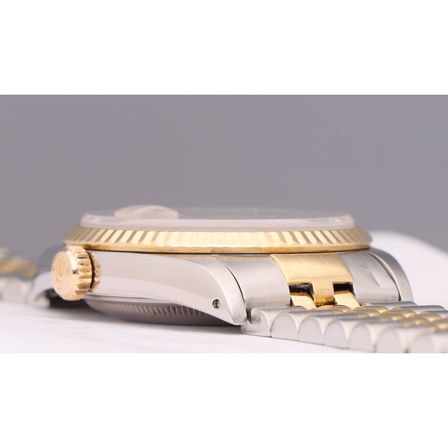 Close-up of a two-tone luxury wristwatch showing a gold fluted bezel and gold center links against a silver body and bracelet outline
