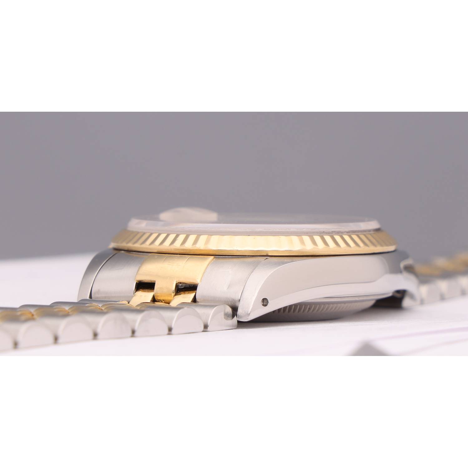 Close-up of a two-tone wristwatch (gold bezel with silver band) lying on a white surface, focusing on the beveled bezel and bracelet links