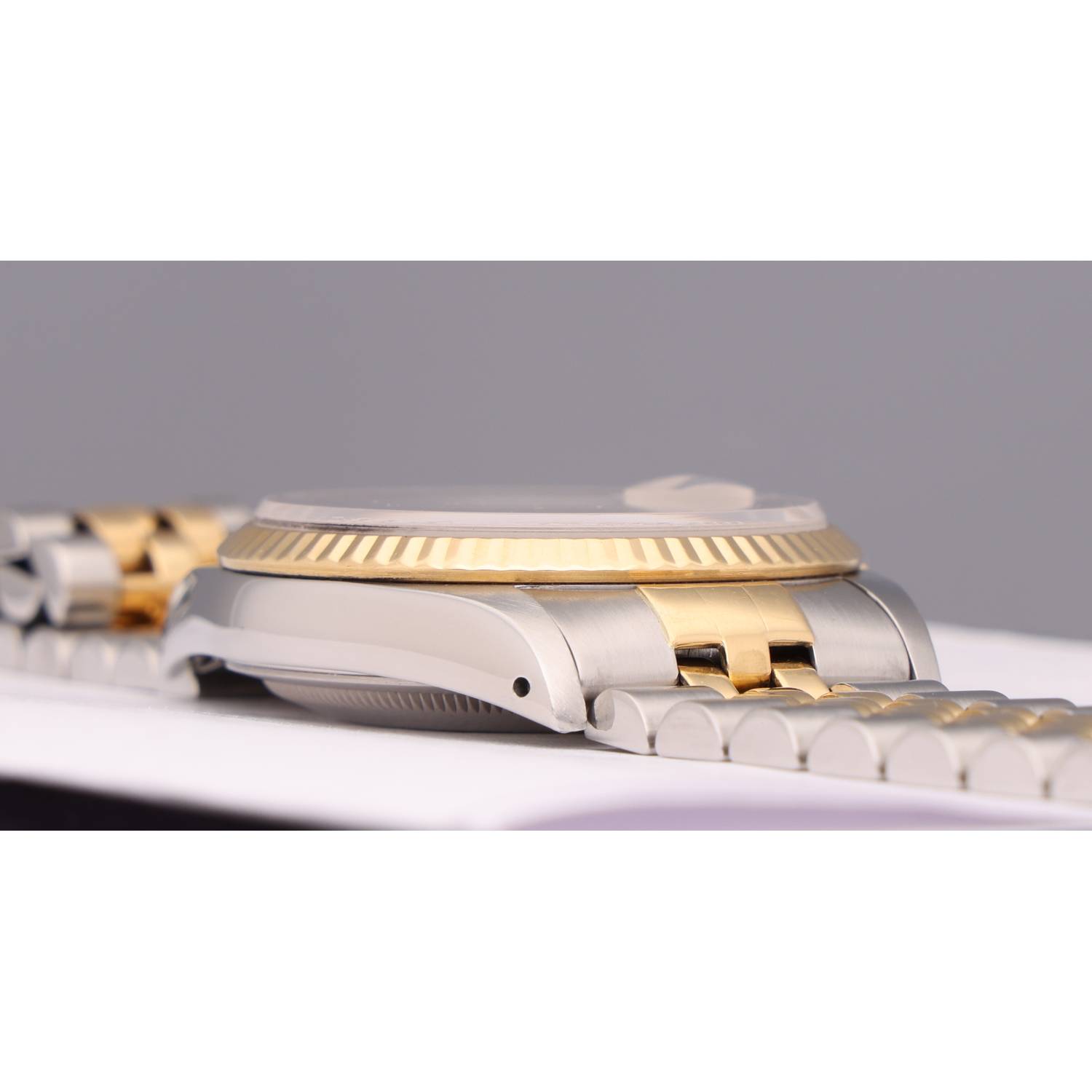 Close-up of a two-tone wristwatch with a gold fluted bezel and silver case on a white surface