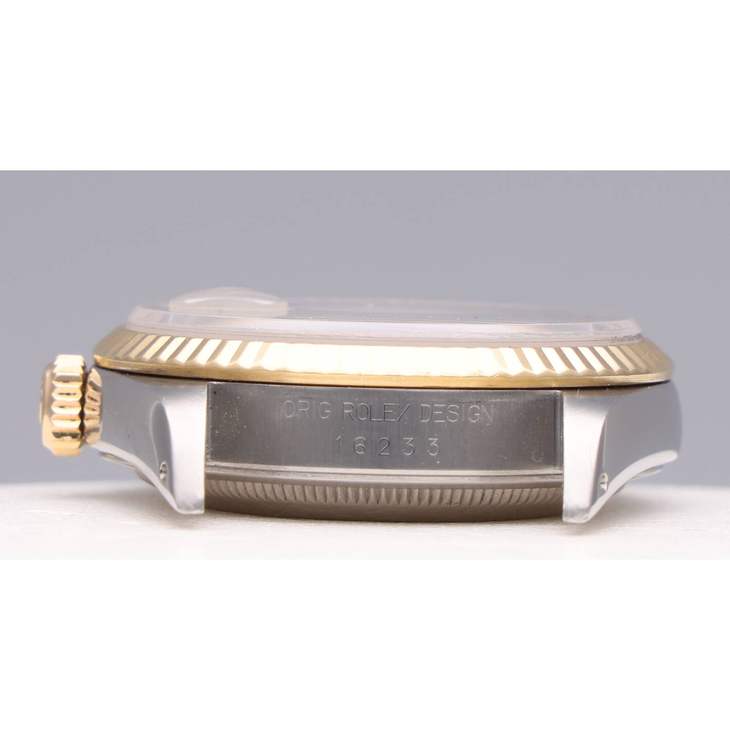 Close-up of a Rolex watch side with a gold fluted bezel and engraved 'ORIG ROLEX DESIGN 16233' on the case.