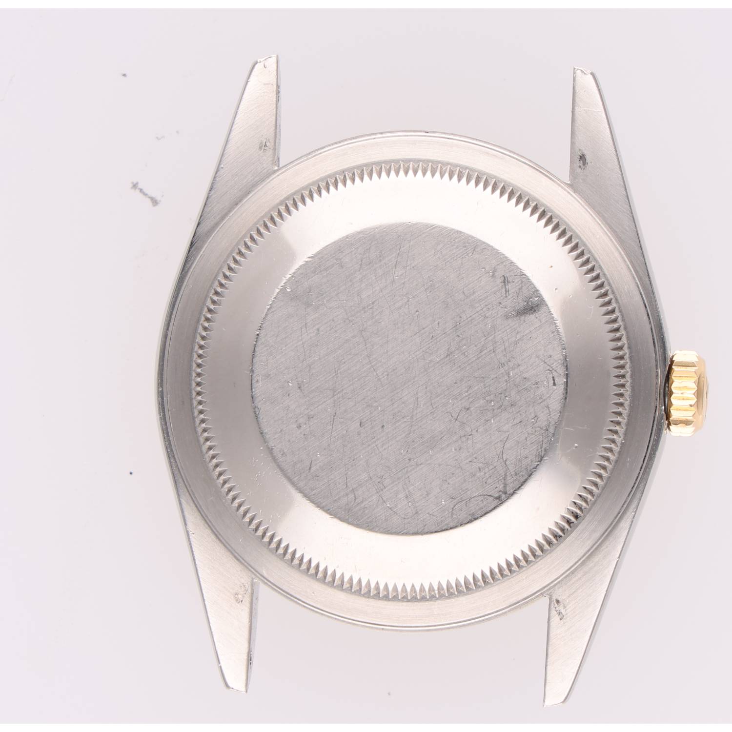 Back of a metal wristwatch showing the screw-down case back with a textured edge and crown on the right; no dial visible.
