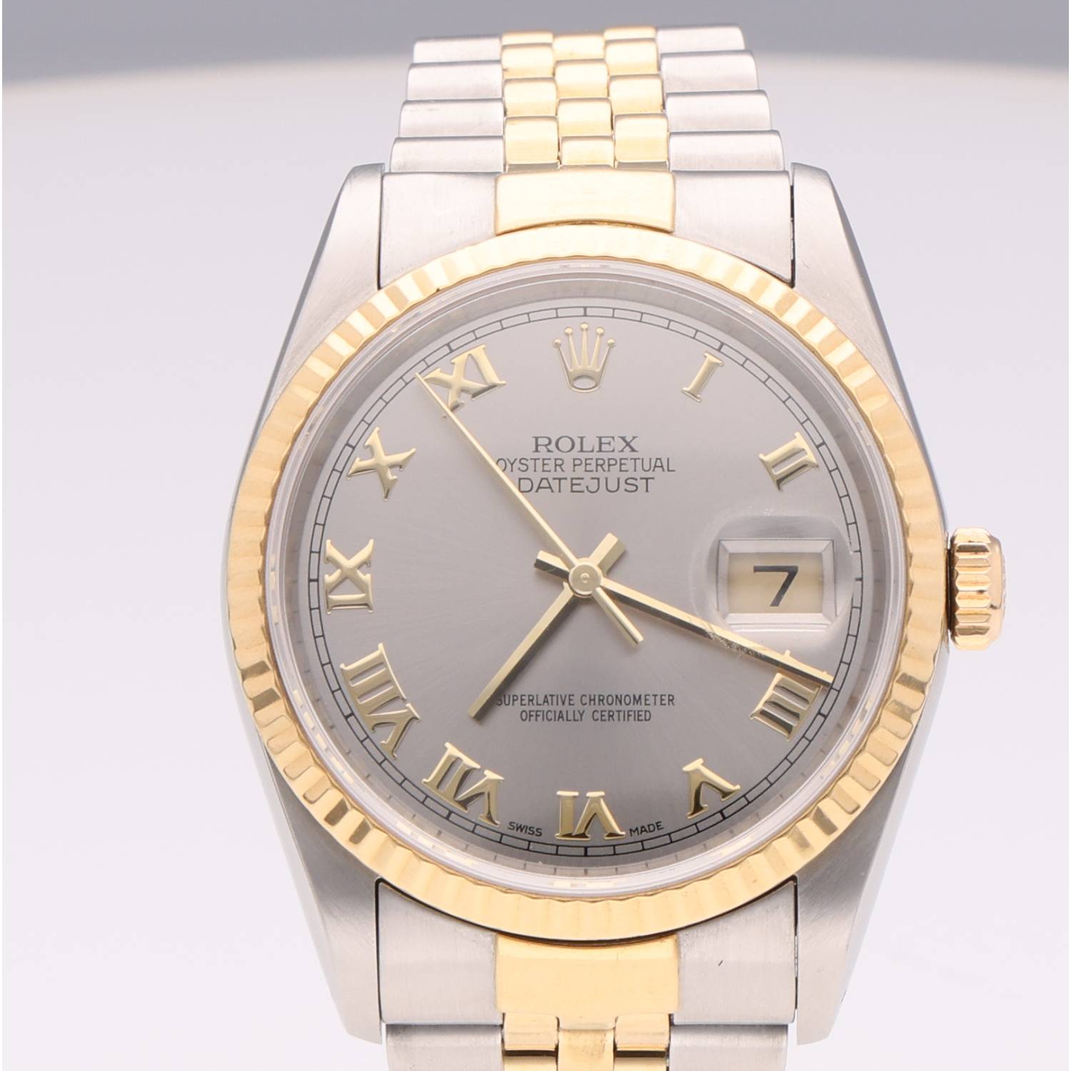 Close-up of a two-tone Rolex Oyster Perpetual Datejust watch: silver dial, gold Roman numerals, gold bezel, and two-tone bracelet with a date window at 3 o'clock.