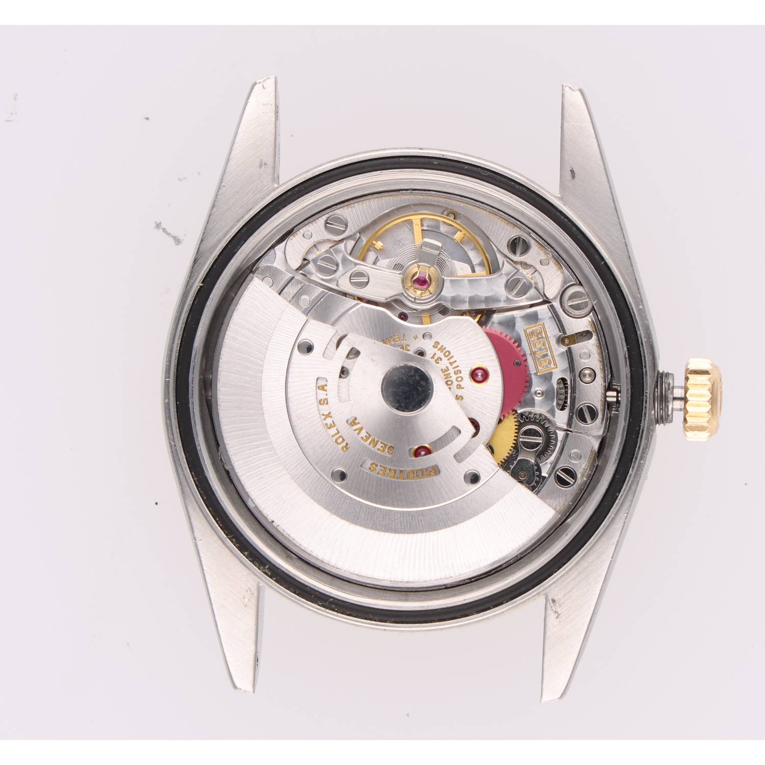 Back view of a mechanical wristwatch movement with rotor, gears, and red jewel bearings visible inside a silver case. A gold crown is on the right.