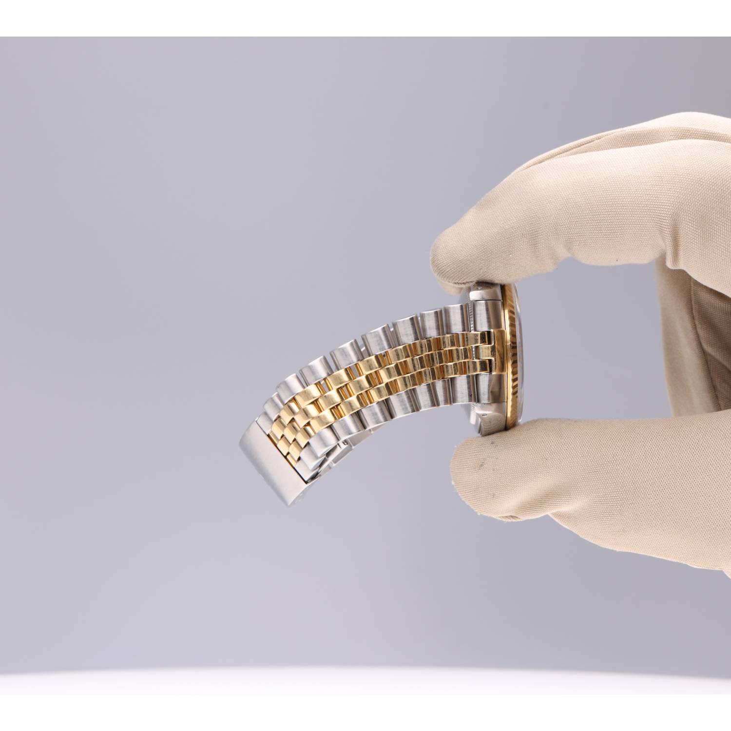 Gloved hand holds a two-tone gold and silver metal watch bracelet.