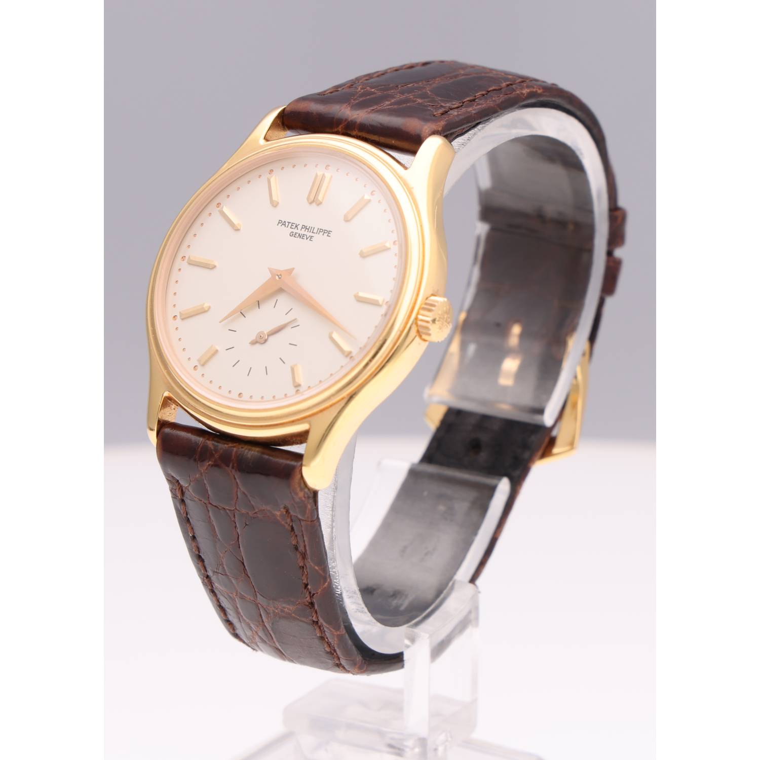 Gold-tone Patek Philippe wristwatch with a white dial and brown leather strap on a display stand.