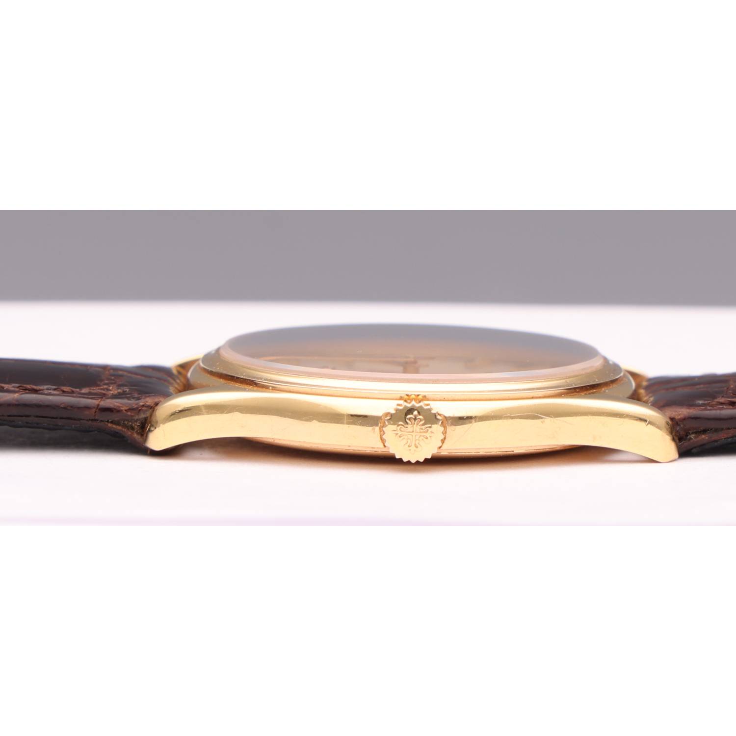 Close-up side view of a gold wristwatch with a leather strap and a decorative crown at the crown area