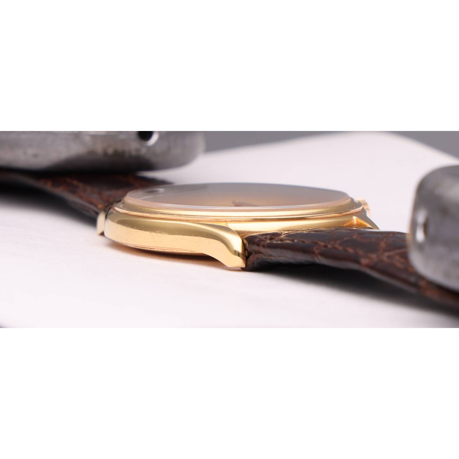 Close-up of a gold wristwatch with a brown leather strap on a white surface